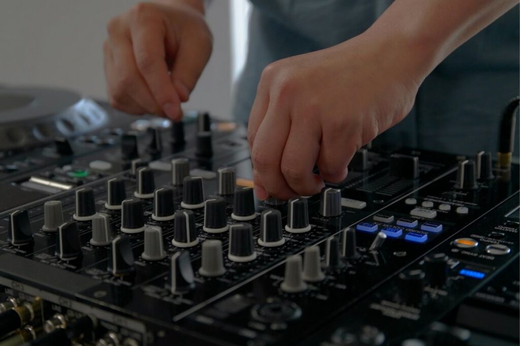 Hands on a DJ mixer at Drop Studios